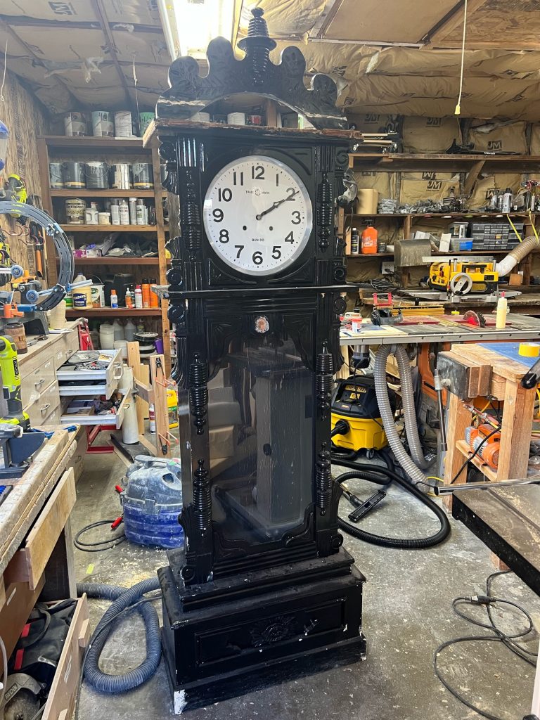 a grandfather clock that has been painted black, placed in a workshop