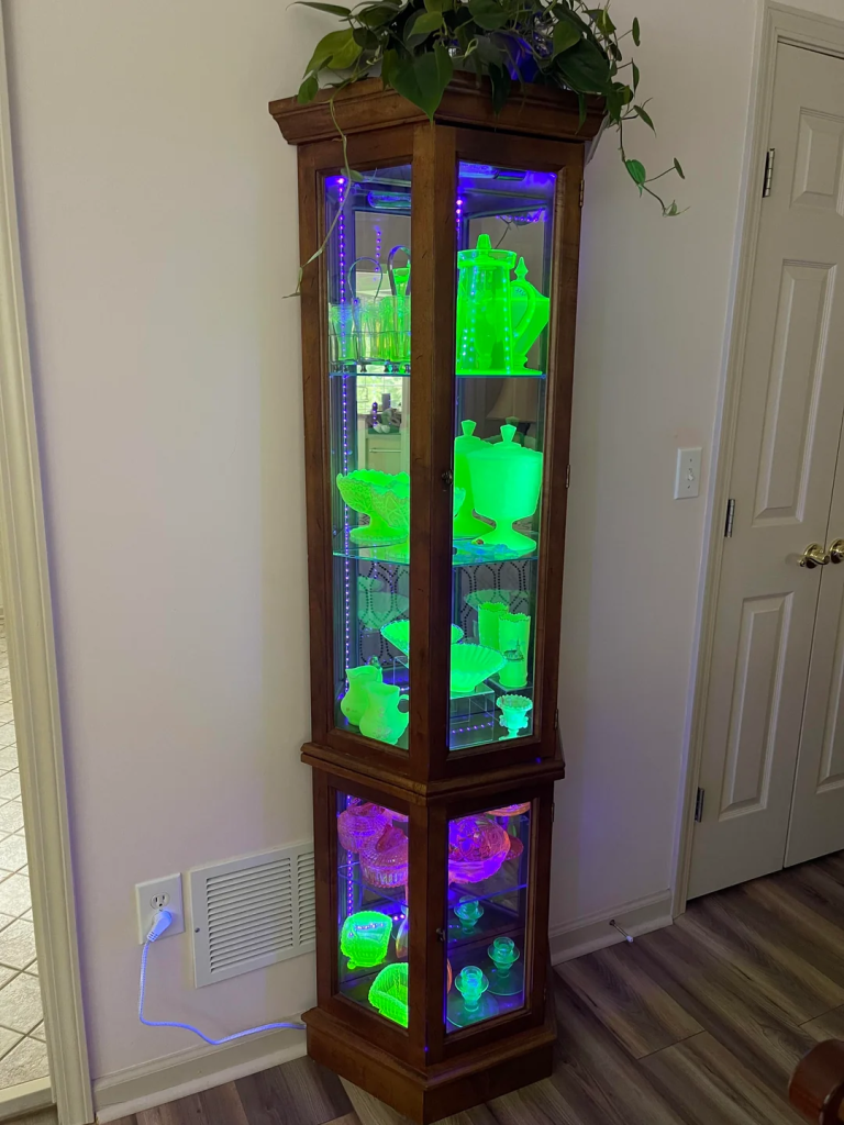 a display cabinet full of glowing uranium glass under a blacklight
