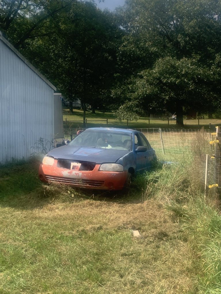 an old broken down looking car abandoned in a yard