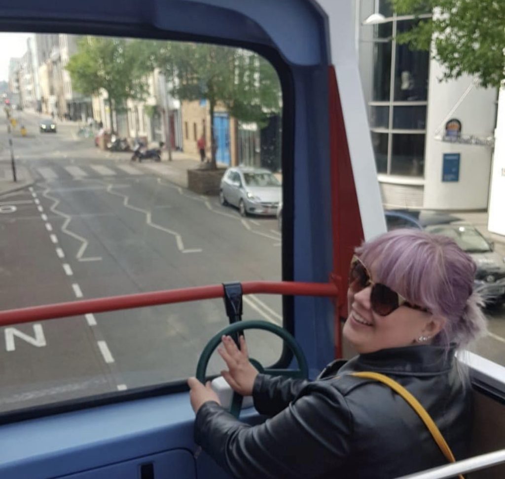 A woman on the top deck of a double decker bus pretending to drive the bus