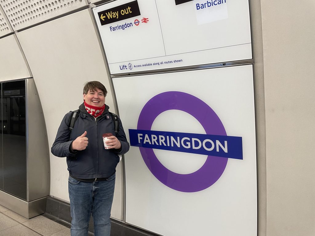 A man standing in front of a London tube stop sign