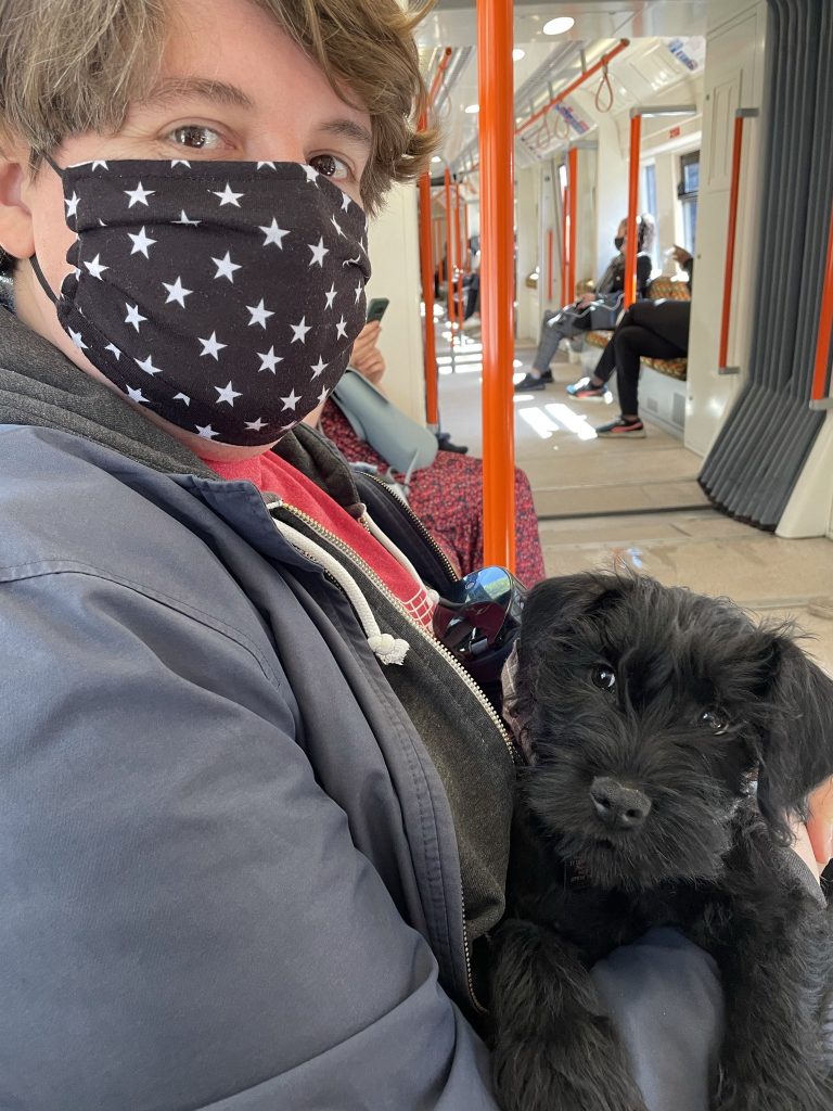 A masked man holding a black dog on the London tube