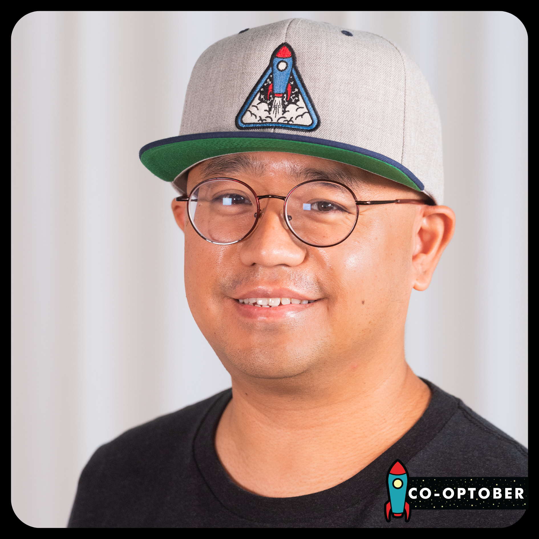 Danny Baruela donning a grey Launch Crew hat with a brim that is navy on top and green underneath. Embroidered in the center is an illustration of a rocket taking off.