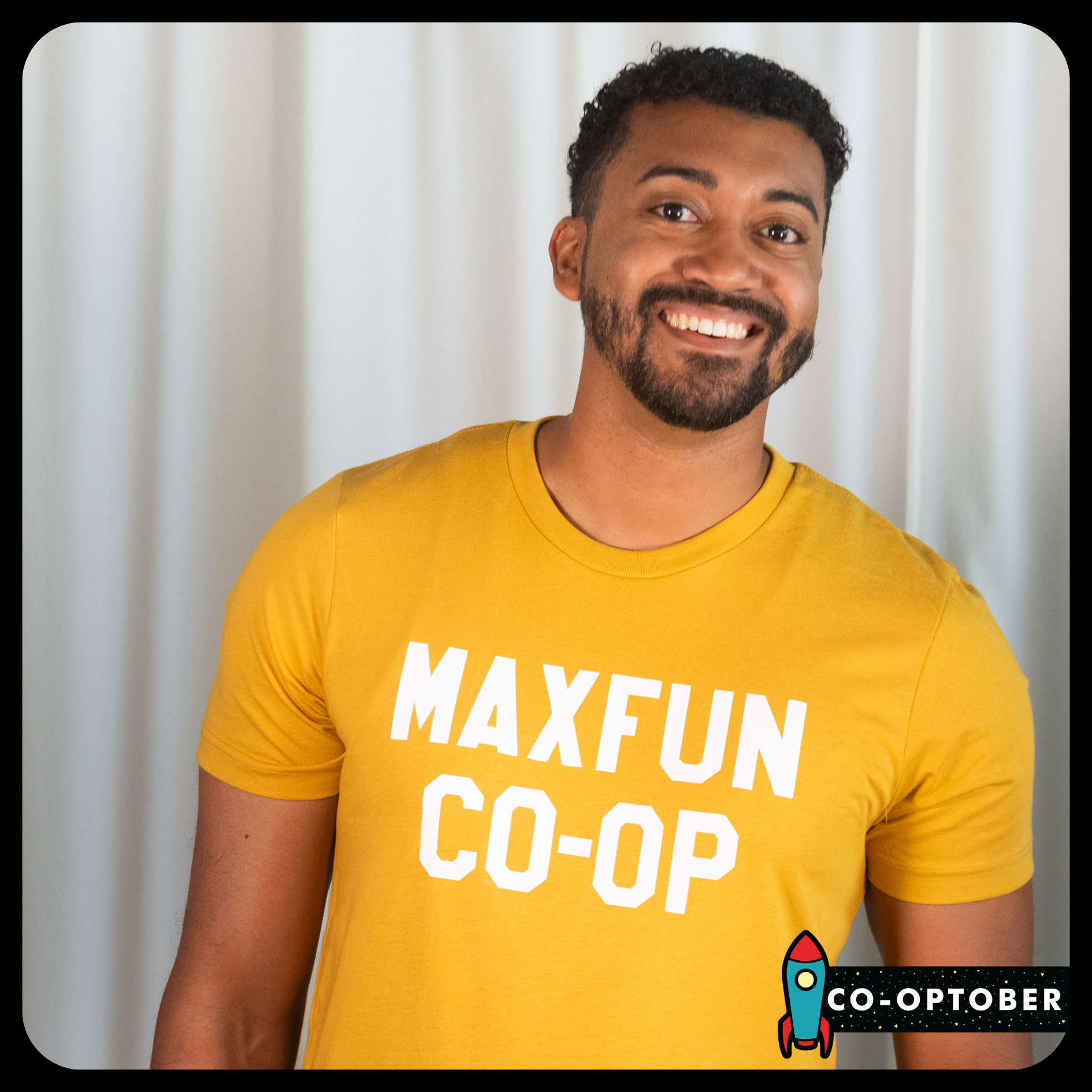 Julian Burrell wearing a mustard colored shirt that reads MaxFun Co-op in white lettering.