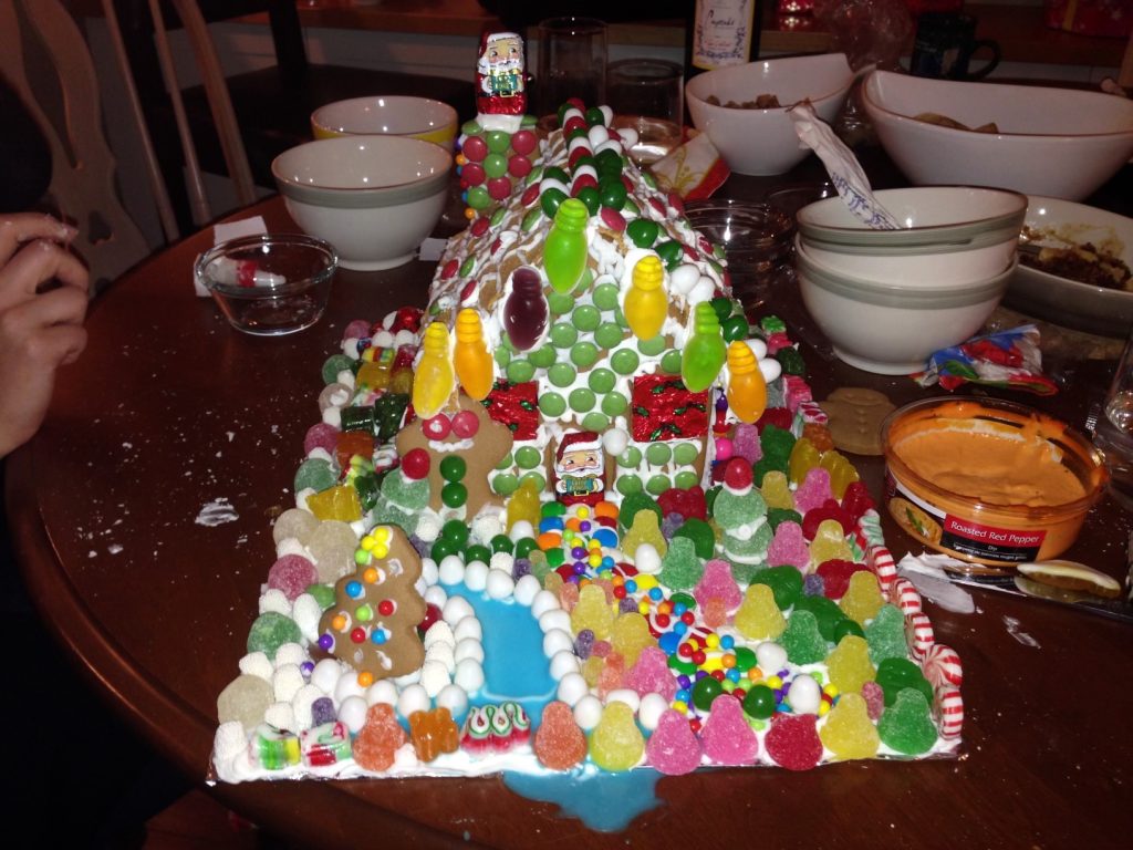 A very haphazard-looking gingerbread house with a blue icing stream dripping off the edge