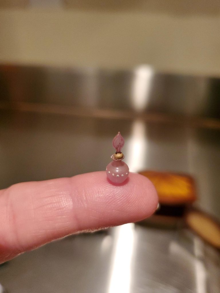 A miniature perfume bottle on a person's fingertip