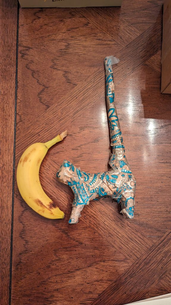 a wrapped present in the shape of a cat with a long tail, next to a banana