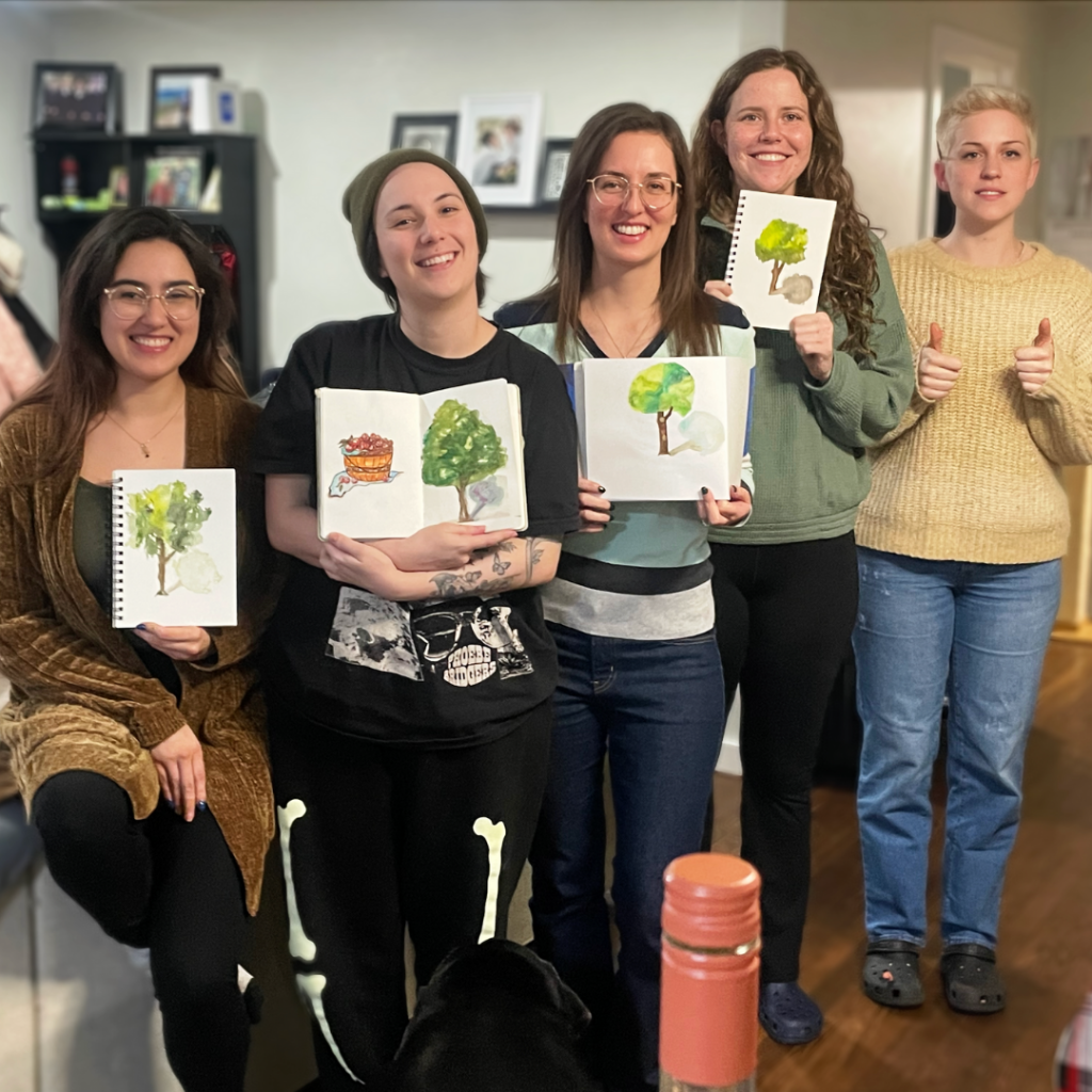 5 women posing together. From left to right, the first 4 have a painting they are showing off. The 5th woman on the right is not holding a painting but has both thumbs up.