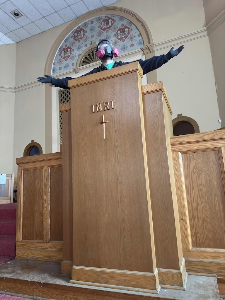 A man at a church pulpit wearing a safety respirator mask
