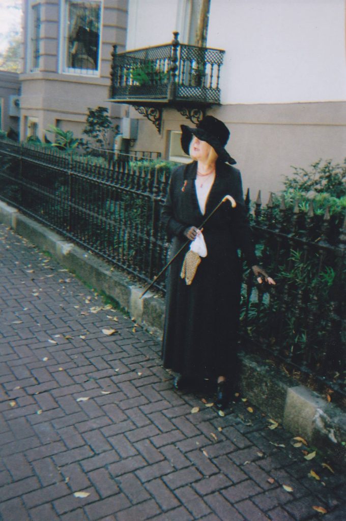 A woman dressed in all black, with a black hat and cane