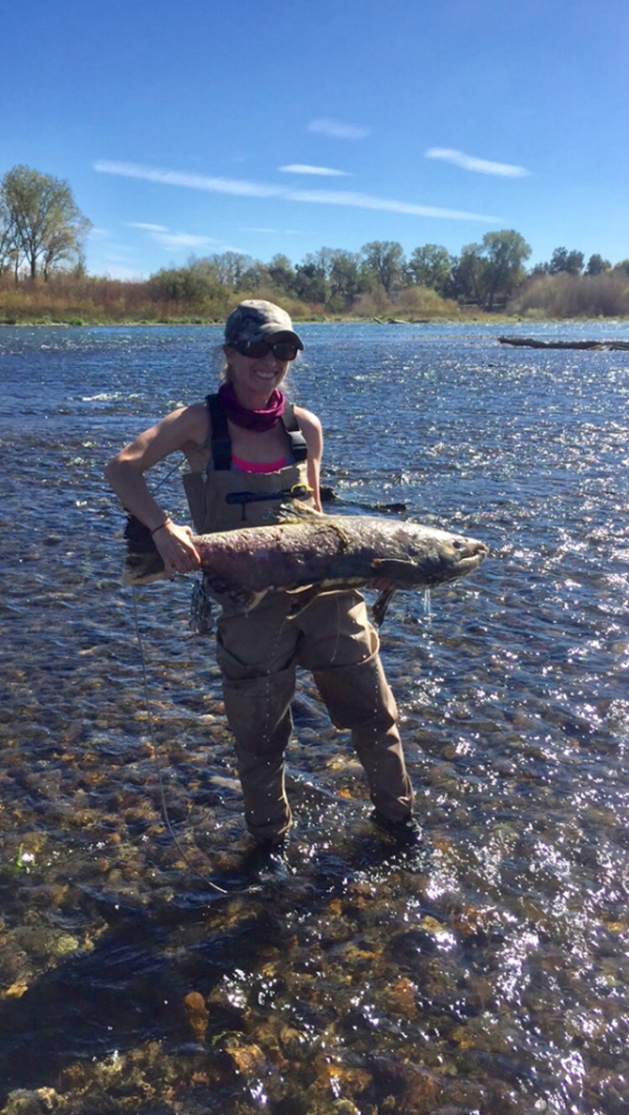 A woman standing in a river holding a salmon
