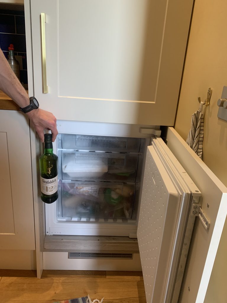A bottle of Glenfiddich being held up to a small open freezer