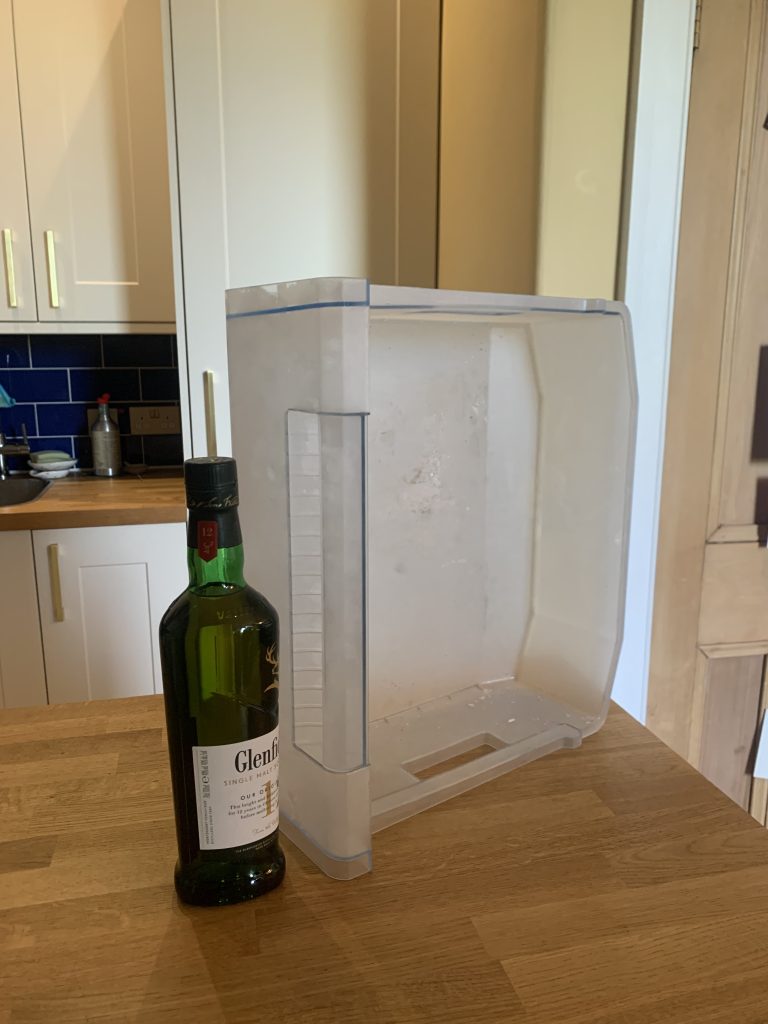 An empty freezer drawer on its side, with a bottle of Glenfiddich next to it