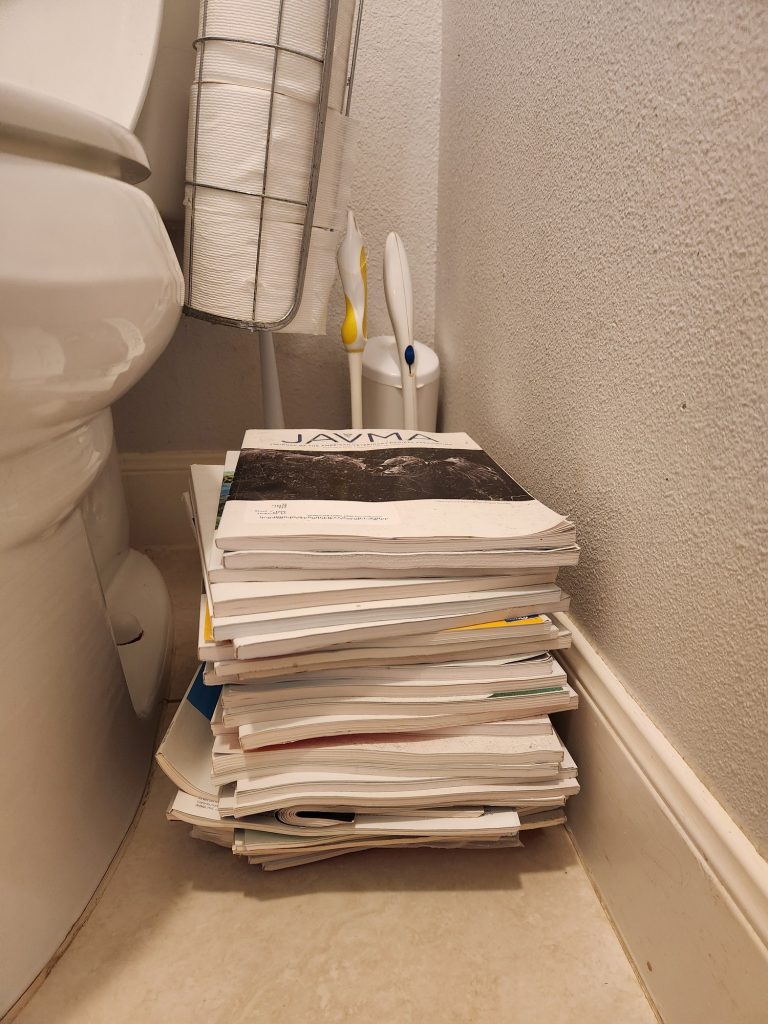 A stack of magazines next to a toilet that is so high, it reaches the bottom of the bowl.