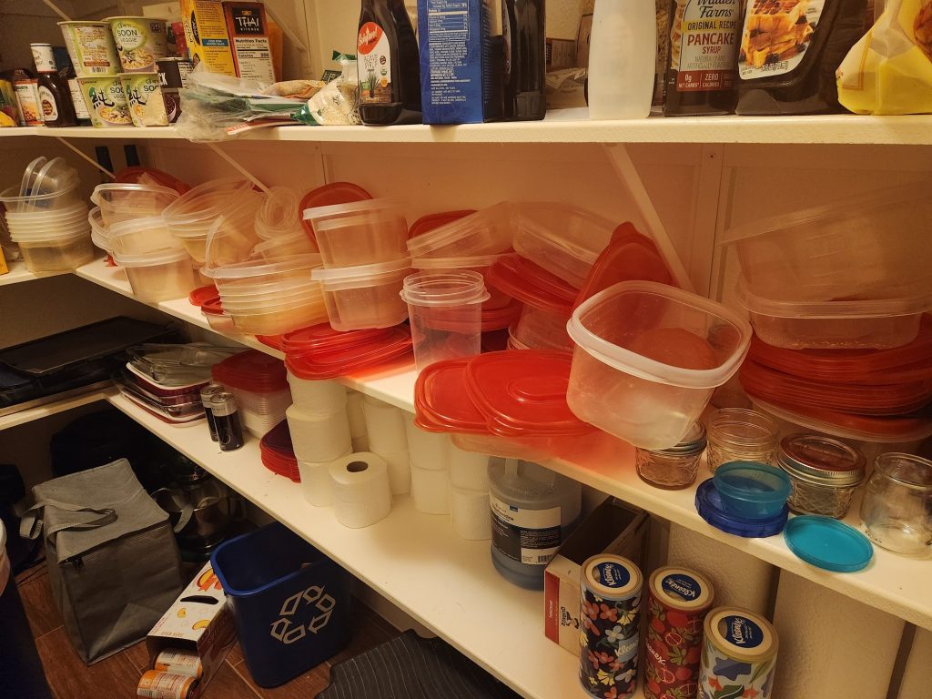 A shelf of plastic food storage containers and lids, with zero organization