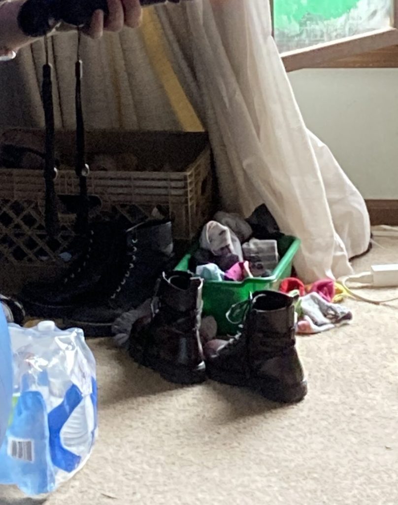 A green bin on the floor with socks in and around it, next to some shoes, and a flat of water bottles