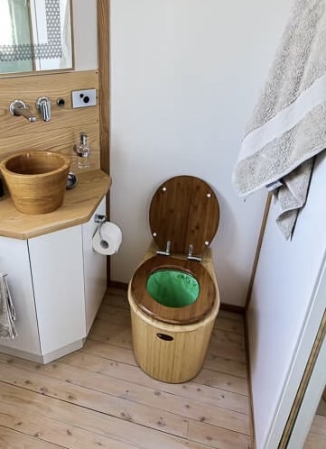 A toilet that is essentially a bucket inside another one, with a green liner bag and a dark wooden toilet seat