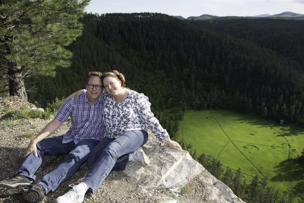 A couple sitting on a cliff above a grassy field