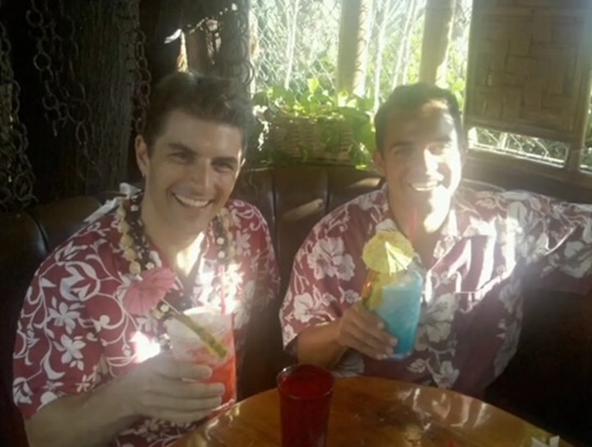 Two men wearing aloha shirts, posed together and smiling