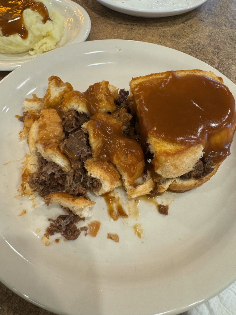 A sandwich that has been covered in gravy, that has been cut up in order to eat with a fork.