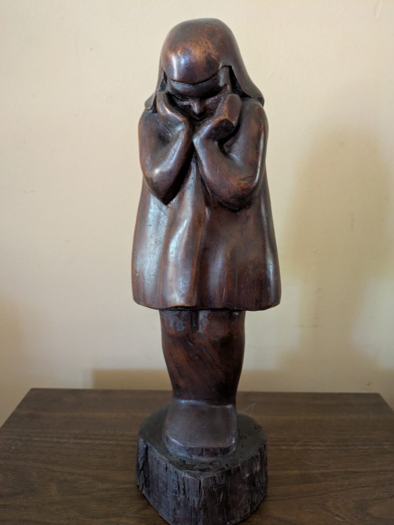 A wooden sculpture of a girl with her hands holding her face, as she looks down
