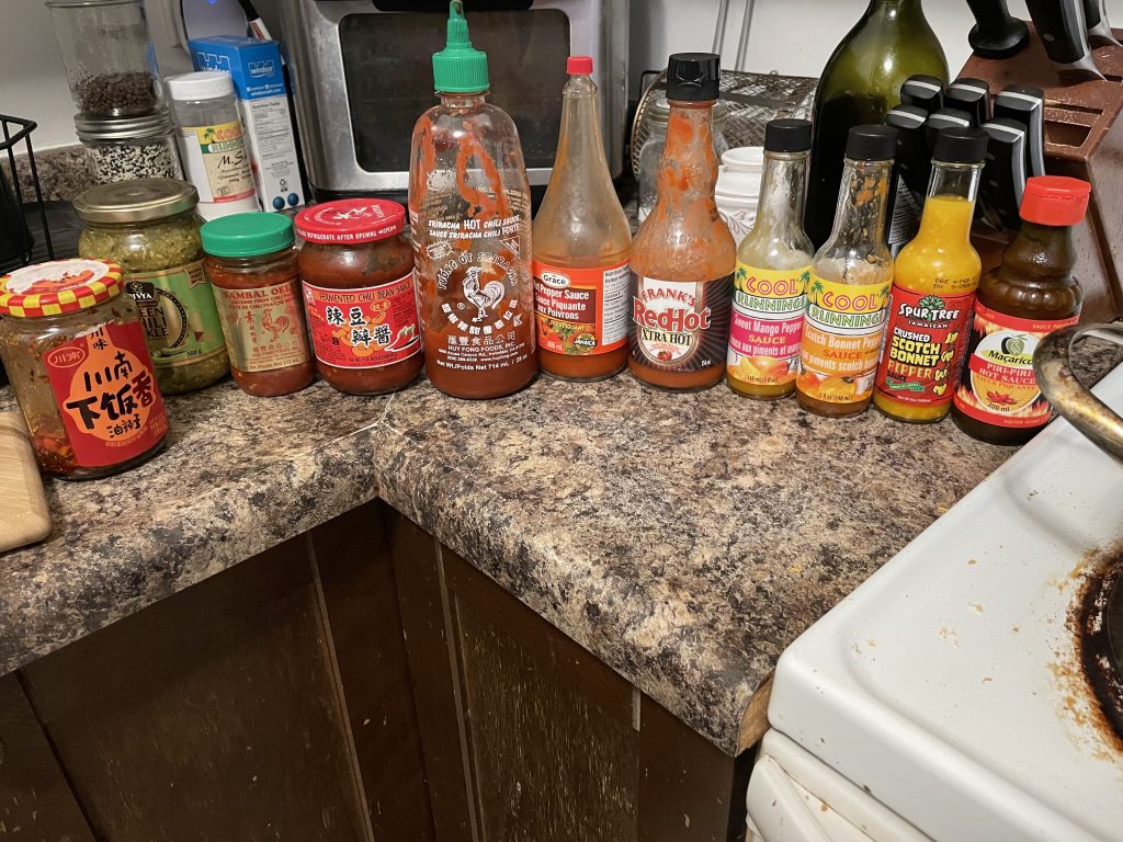 a bunch of different types of hot sauce lined up on a kitchen counter