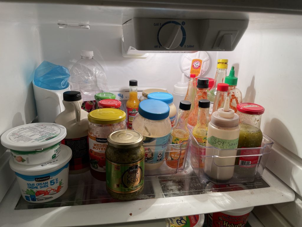 Top shelf of a refrigerator with sauces in two large clear plastic containers