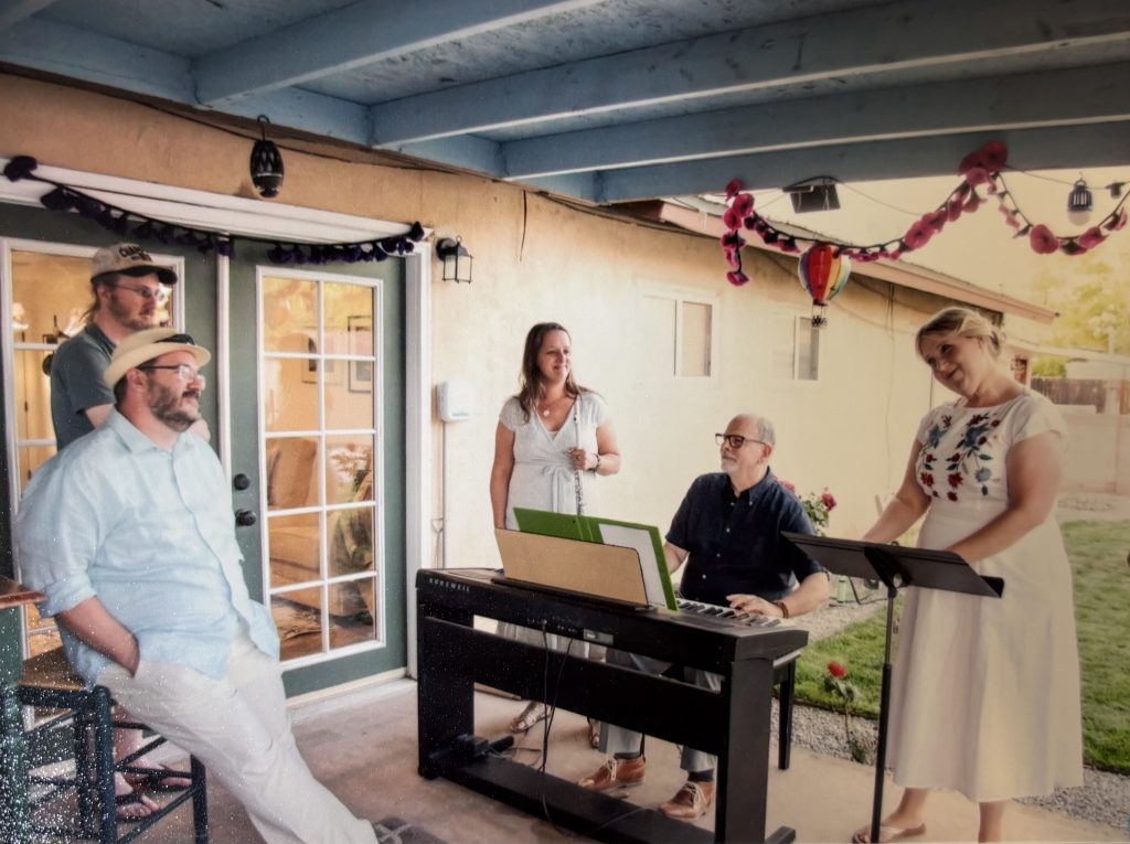A groups of people standing around an electric piano in a backyard patio