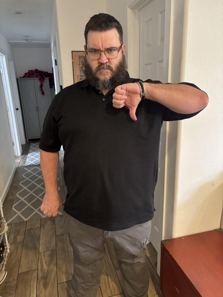 A man wearing a black polo shirt and gray pants giving a thumbs down gesture
