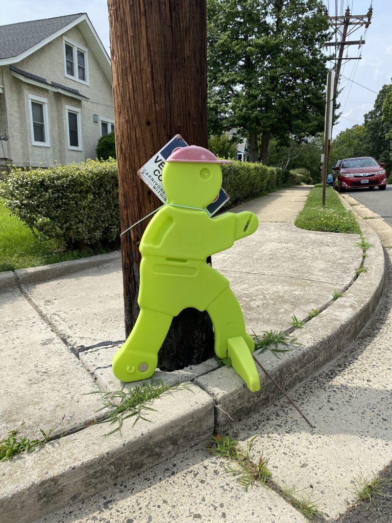 A neon green plastic traffic sign tied to a wooden utility pole that is a figure with a red cap