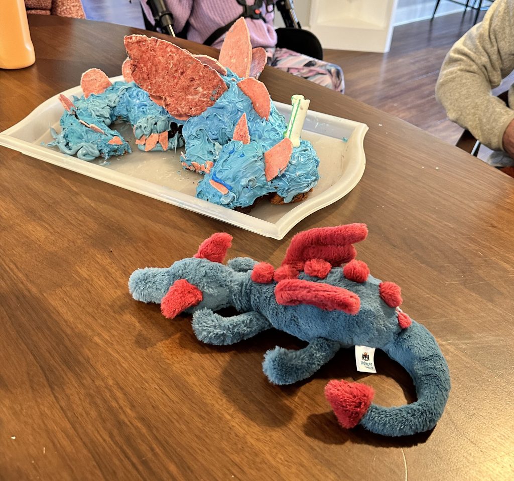 A blue dragon stuffy next to a cake that looks like it