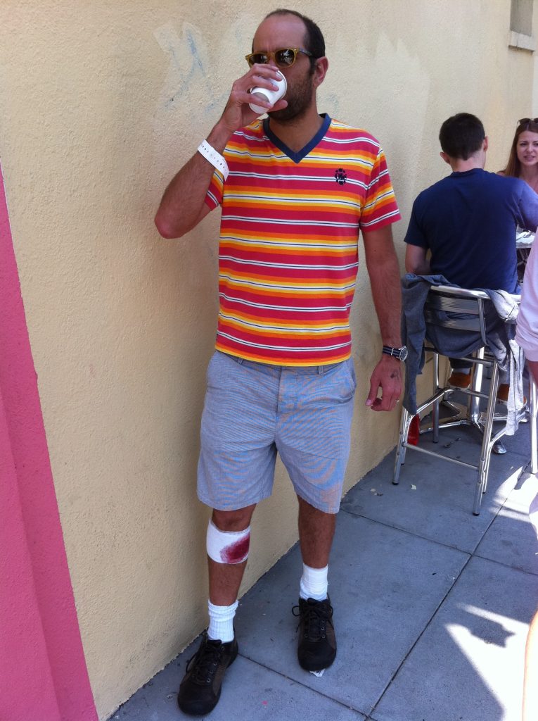 A man holding a drink and bandages around his leg and wrist