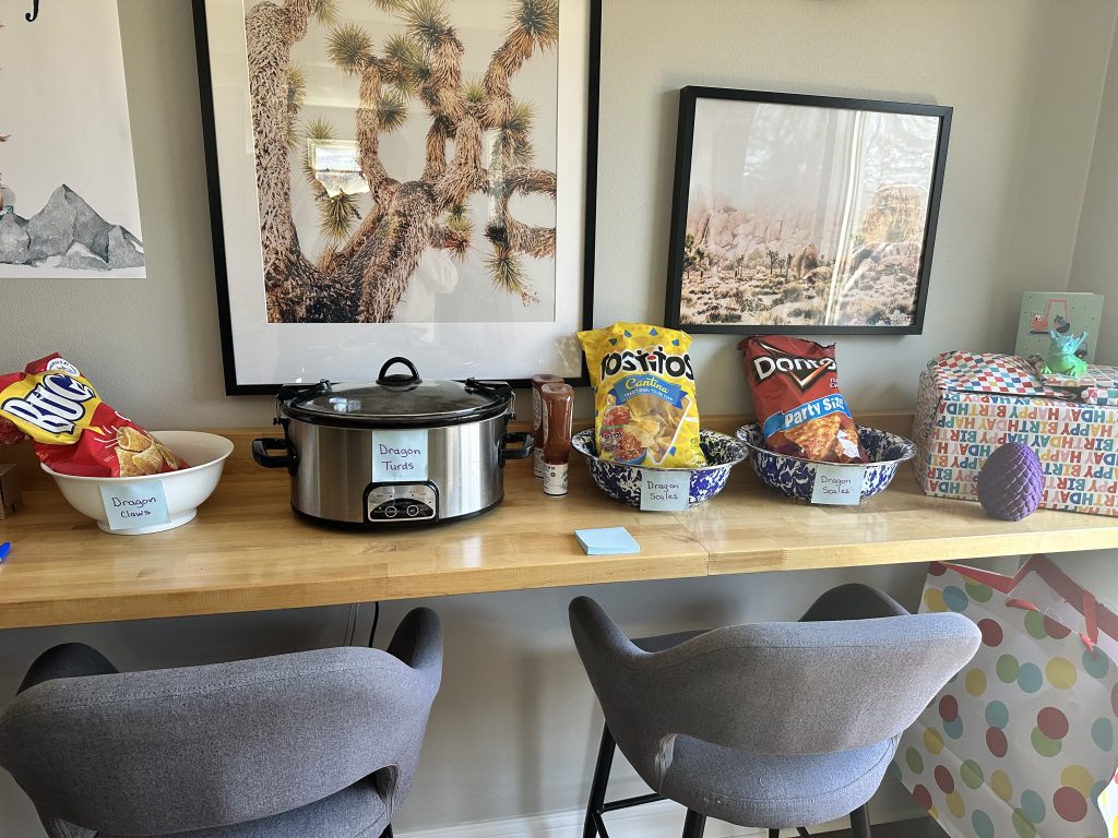 A table with a crock pot and chips on it. The crockpot has a label that says 
