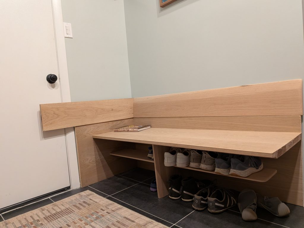 a wooden built in shoe shelf in an entryway. Part of the shelf seems to be extending over the door.