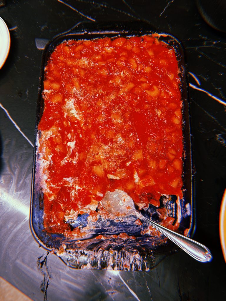 A baking dish with food it. The top layer is a red jello with cut up strawberries in it.