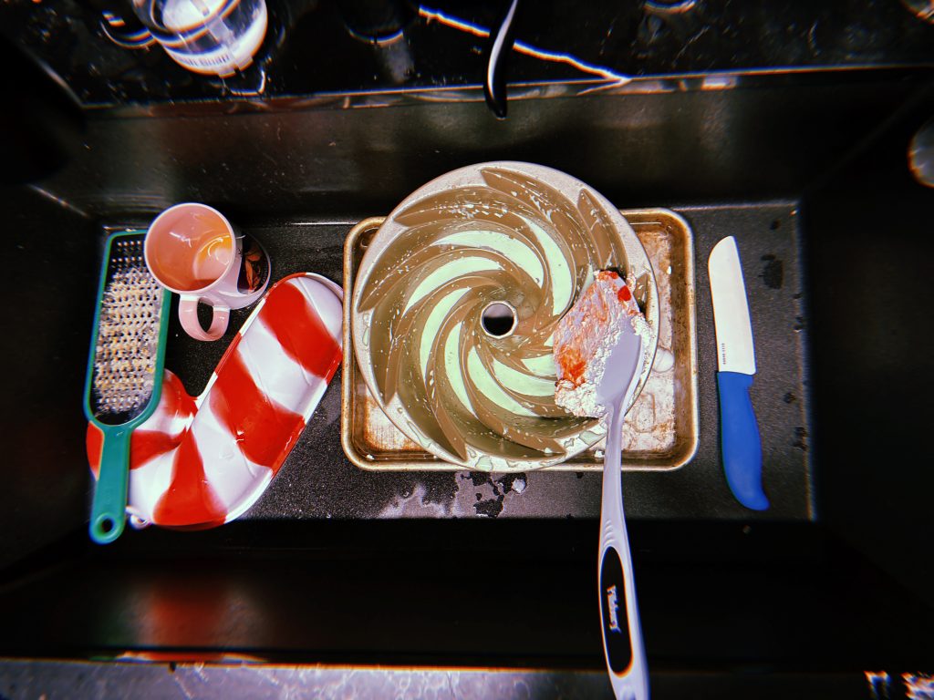A sink with dirty dishes including a cake mold with mint green jello remnants in it.