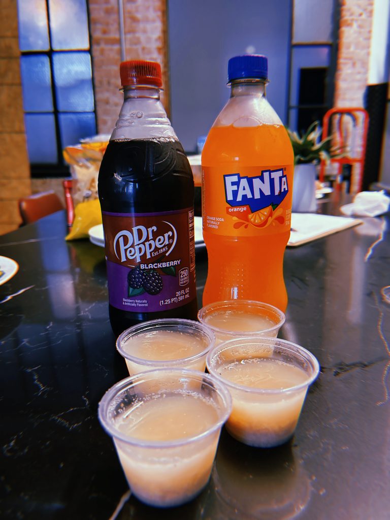 Four off-white jello shots in front of a bottle of Blackberry Dr Pepper and Orange Fanta