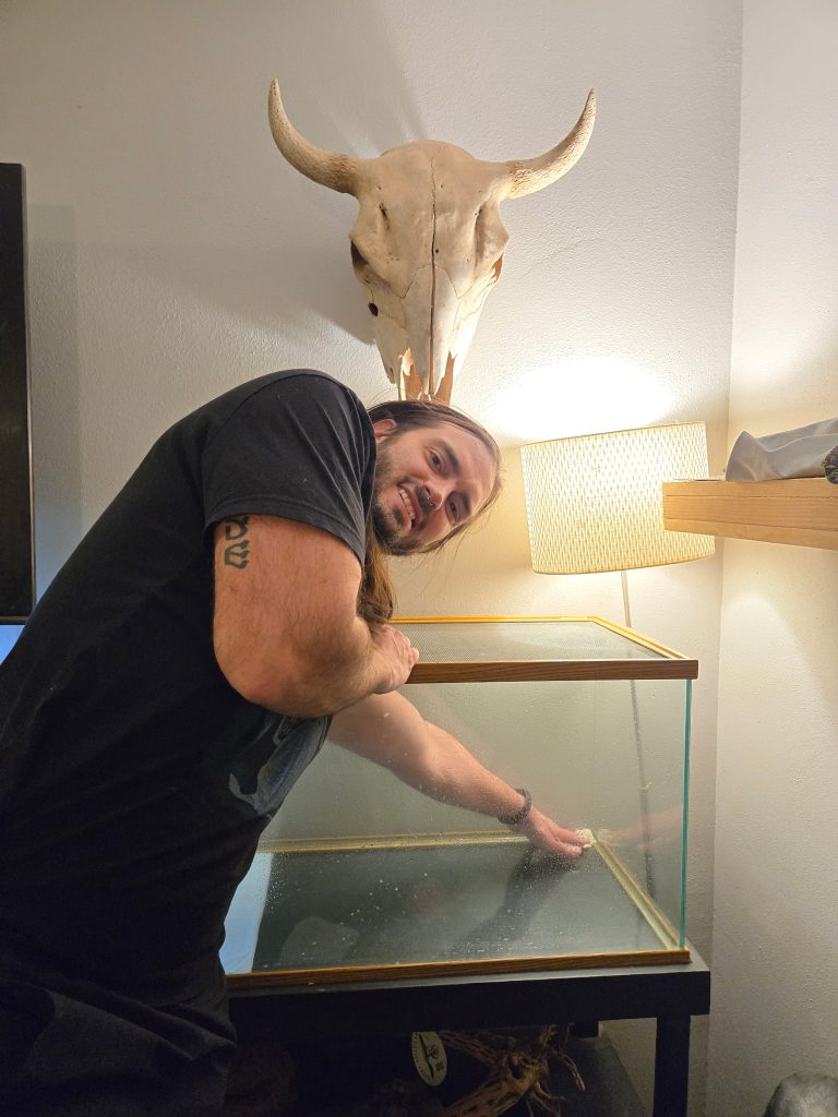 A man with his arm in a large, empty reptile tank