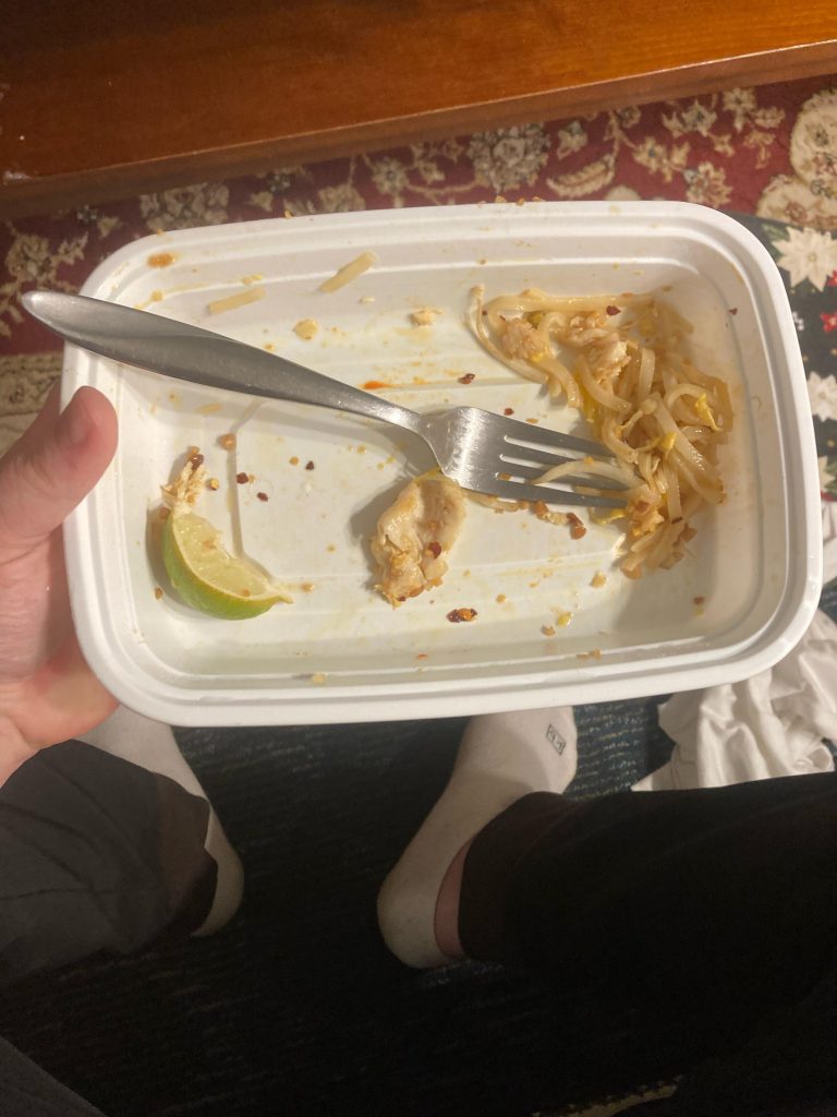 a white plastic take out container with one bite of noodles in the corner of it.