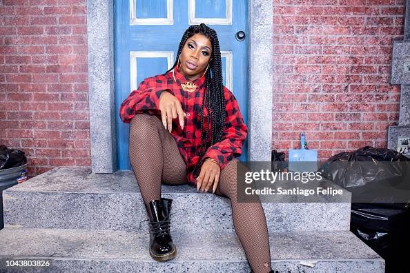 Monét X Change wearing a buffalo plaid dress, rights, and Doc Martens, sitting on an artificial stoop at Drag Con