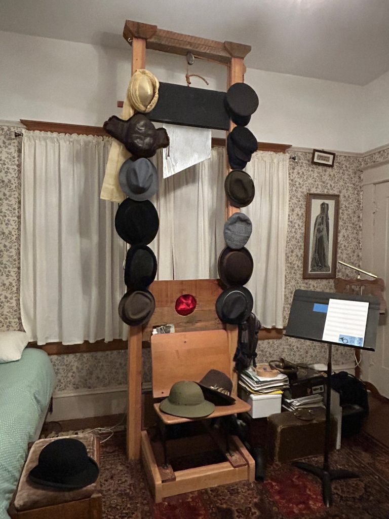 A nearly full sized guillotine with a blade made of wood in a bedroom. Hats are hung on it.