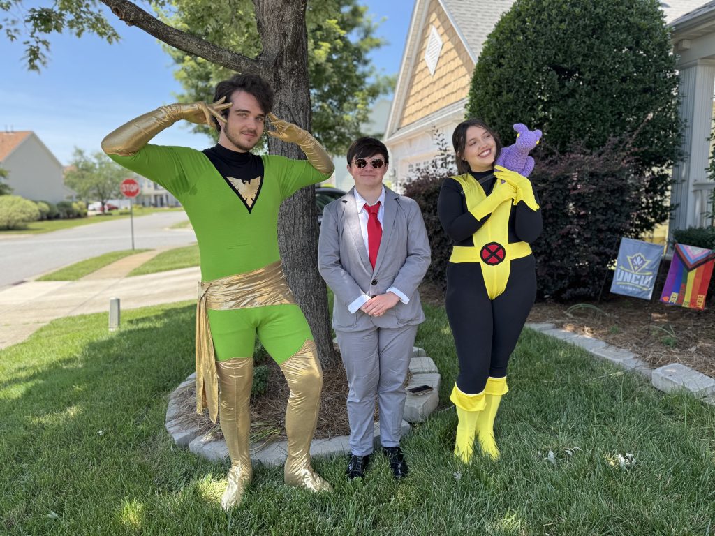 Three young adults in comic book related costumes, posing in a front yard