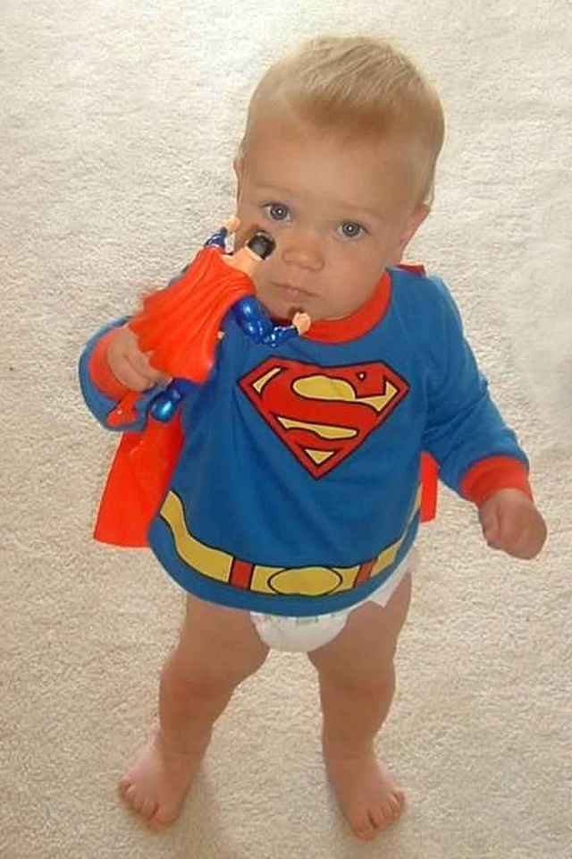 A toddler wearing a superman shirt and cape, holding a Superman action figure