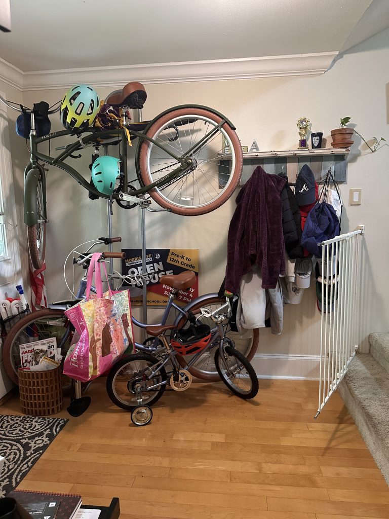 A foyer with bikes being stored, coat hooks on the wall, leading to a staircase and a powder room next to the stair case