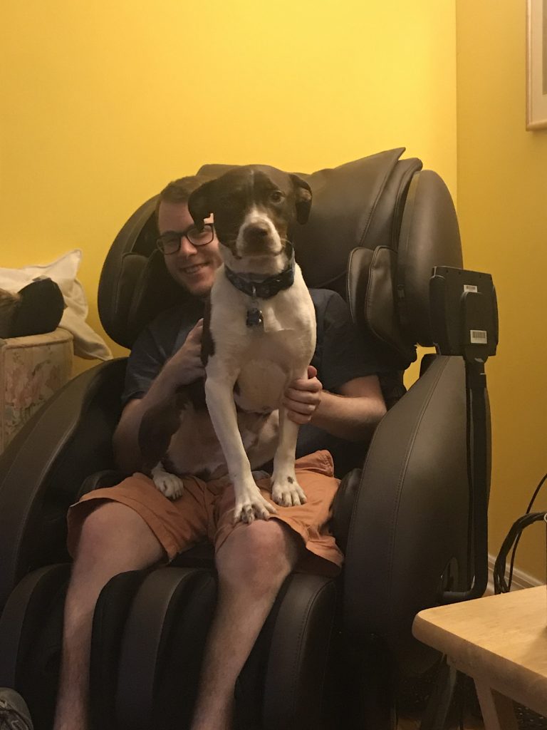 a man and a dog sitting in a large massage chair that is placed in a home living room