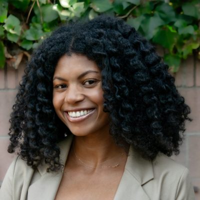 A photo of Shelby smiling and wearing a tan blazer