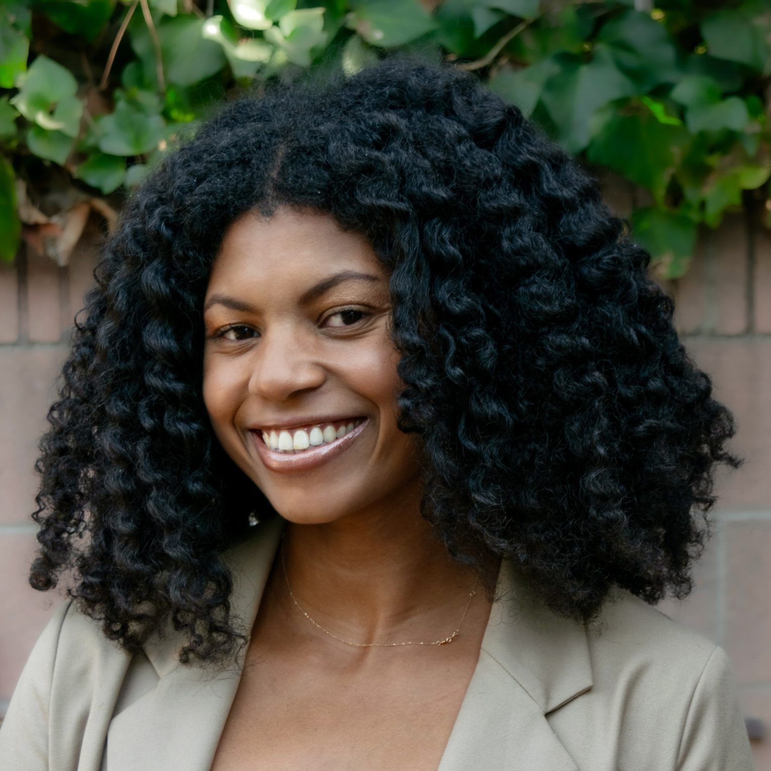 A photo of Shelby smiling and wearing a tan blazer