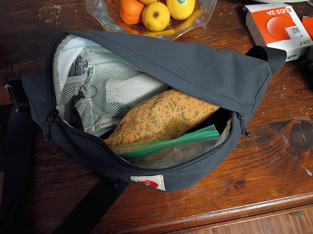 An open fanny pack on a table with a plastic bag of kibble inside it