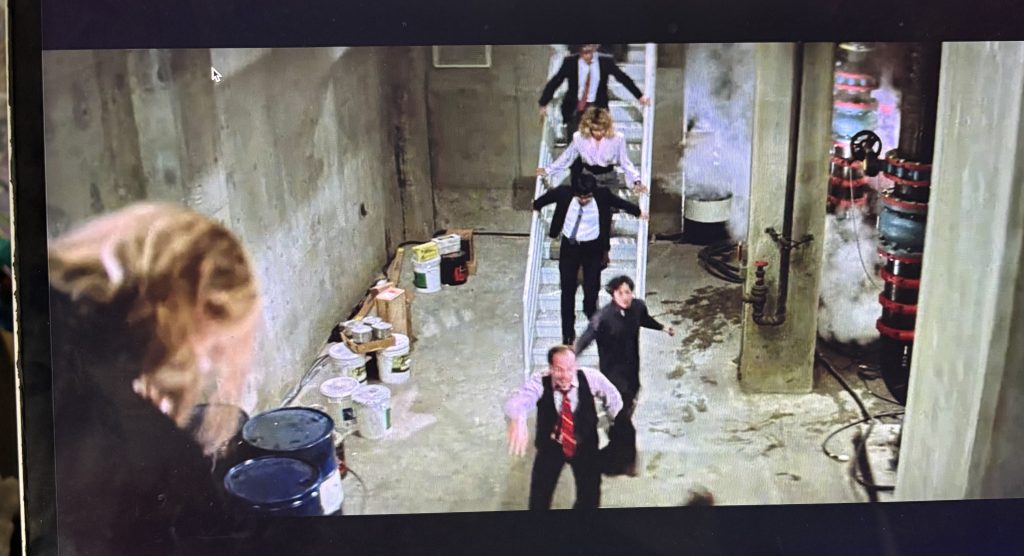 A scene from DIE HARD where Karl is hanging in the foreground and the hostages are running in the background